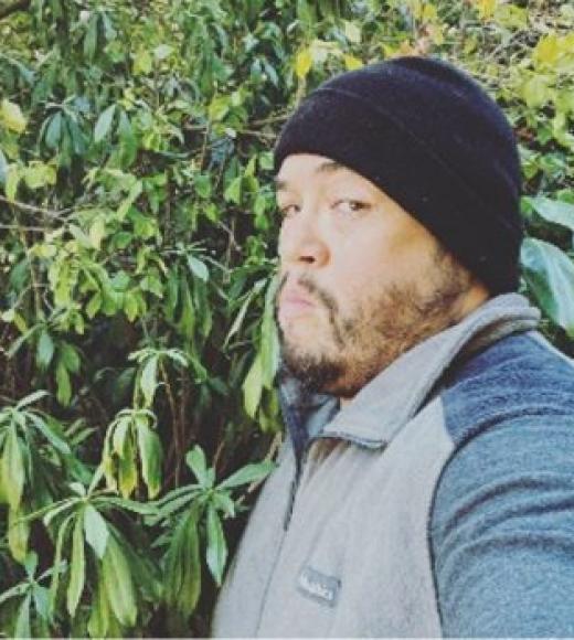 Man wearing a black beanie standing in front of a green bush
