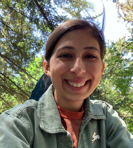 Photo of Emi Marrujo. Her hair is pulled back, and she is wearing an olive green jacket with a bunny rabbit pin.