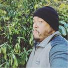 Man wearing a black beanie standing in front of a green bush
