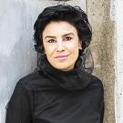 close-up photo of Dena Al-Adeeb in front of a gray backdrop. She is wearing a black top and smiling faintly.